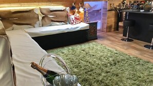 Una habitación acogedora con cama, una alfombra mullida color verde, una zona de bar con taburetes y una botella de champán sobre una bandeja.