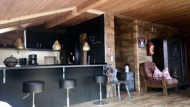 Una cocina moderna con barra, techo de madera y una zona de estar acogedora con una silla estampada.