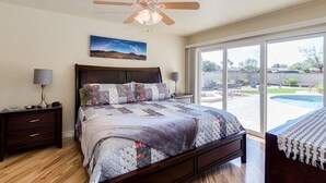 A bedroom with a large bed, a ceiling fan, a nightstand with a lamp, and a view of a swimming pool through a sliding glass door. - PET FRIENDLY IN QUIET NEIGHBORHOOD! (Tempe)