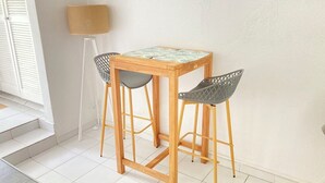 A small wooden table with two chairs, a lamp, and a window with blinds. - Studio Bougainvillier Style Bohème (Marigot)
