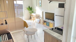 A compact living space with a kitchenette, a dining area with two round tables, a sofa, and a TV. - Studio Bougainvillier Style Bohème (Marigot)
