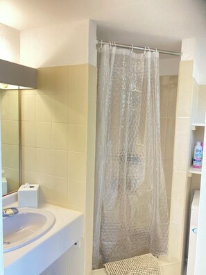 Une salle de bain avec un rideau de douche, un lavabo, un miroir et une étagère contenant des articles de toilette.