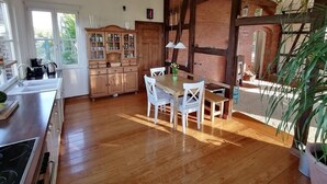 Une cuisine avec un plancher en bois, une table à manger avec des chaises, un buffet en bois et un luminaire suspendu.