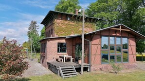 Une maison en briques avec une terrasse en bois, une grande fenêtre et un petit jardin.