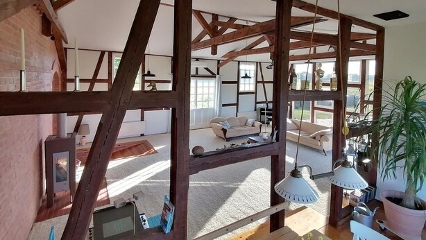 Une pièce spacieuse avec des poutres apparentes, une grande fenêtre et un coin salon confortable avec un canapé et une table.