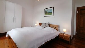 Une chambre à coucher avec un lit, une tête de lit en bois, des tables de chevet avec des lampes, une armoire et un tableau encadré au mur.