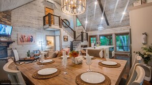 A spacious dining area with a wooden table set for four, surrounded by white chairs. A staircase with a wooden railing leads to an upper level.
