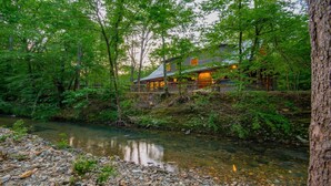 A cabin with a river in front, surrounded by dense forest.
