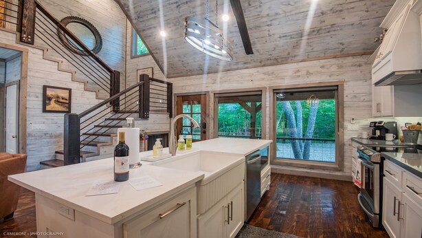 A modern kitchen with a large island, wooden flooring, and a view of trees through large windows.