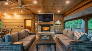 A cozy cabin interior with a stone fireplace, wicker furniture, and a ceiling fan.