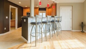 A kitchen with a central island, bar stools, wooden cabinets, and pendant lights.