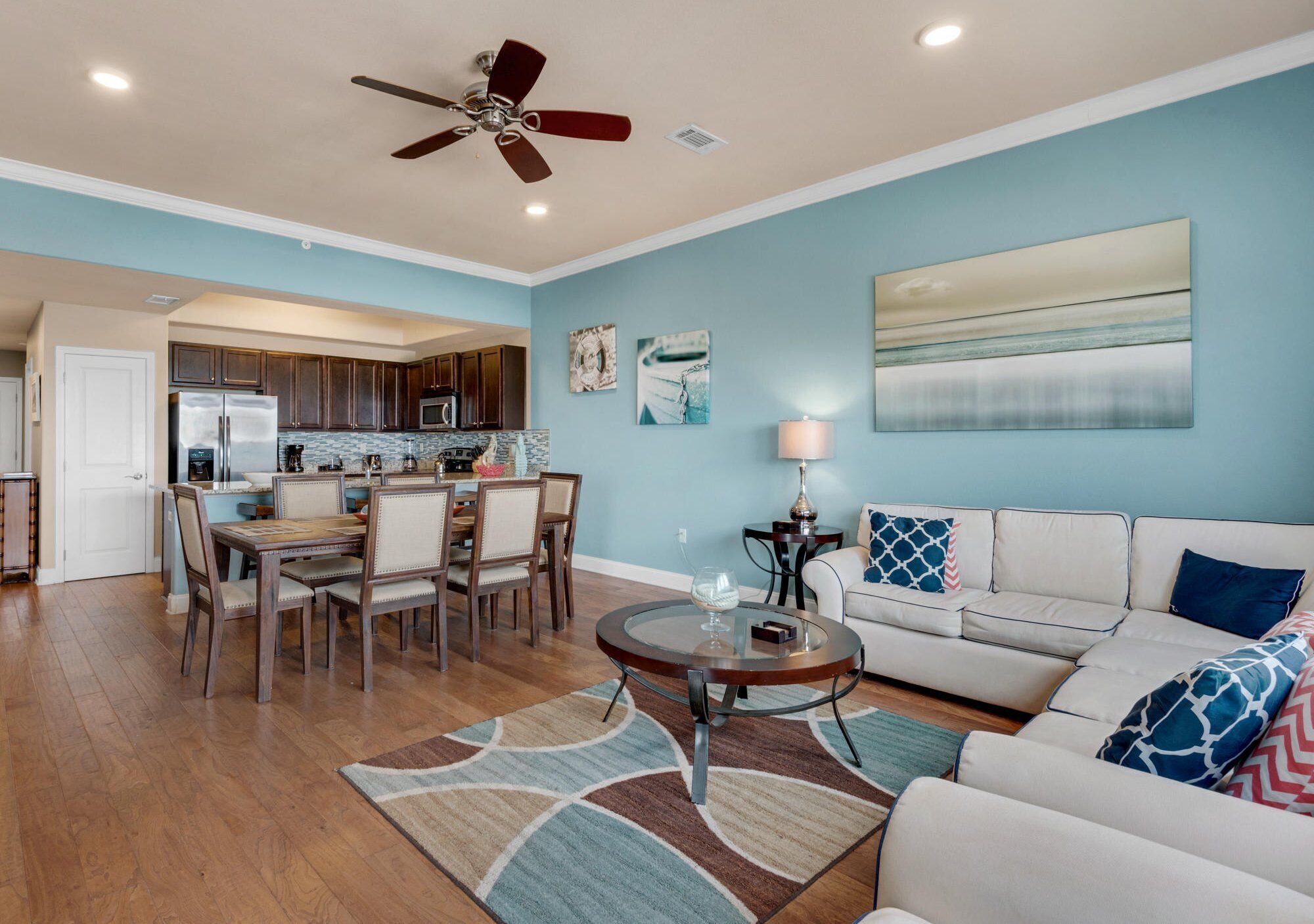 A spacious living room with a dining area, a ceiling fan, and a kitchen in the background.