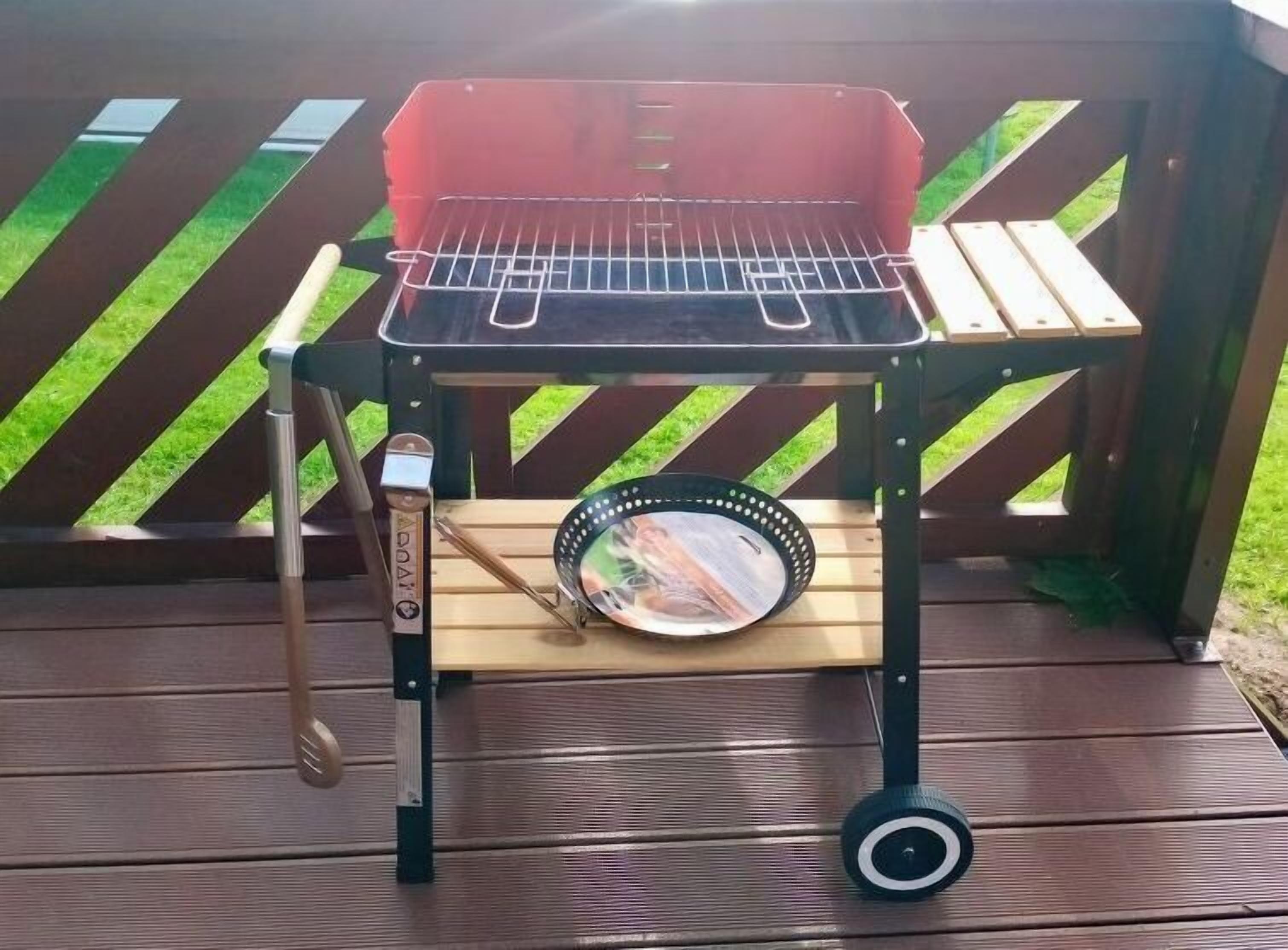 Una parrilla portátil para barbacoa con rejilla metálica, tapa y una pequeña rueda para facilitar su transporte.