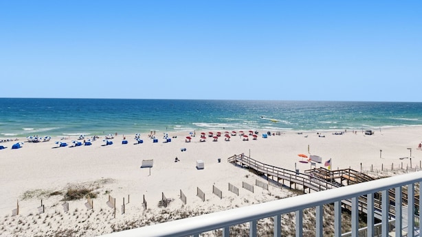 Una playa con un paseo marítimo de madera que conduce al agua, arena y sombrillas.