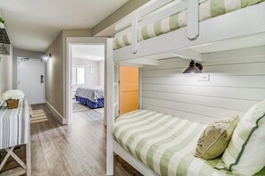 Ein Zimmer mit Etagenbetten, einem Schreibtisch mit gestreiftem Tischlein und einer kleinen Pflanze.