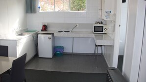 A compact kitchen with white cabinets, a sink, a stove, a microwave, and a small refrigerator. - Taihape Motel (Taihape)