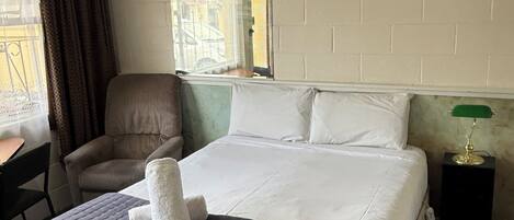 Une chambre d’hôtel avec un lit, une chaise, un bureau, un miroir et une lampe.