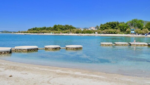 A beach with clear blue water, a sandy shore, and a row of concrete benches. - Luxury Apartments Iva (Vodice)