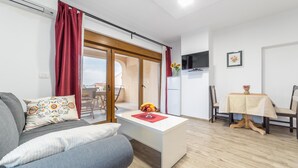 A modern living room with a sofa, a coffee table with a fruit bowl, a dining area with a table and chairs, and a sliding glass door leading to an outdoor space. - Luxury Apartments Iva (Vodice)