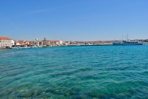 A coastal town with clear blue waters, a large blue boat docked at the harbor, and buildings with red roofs along the waterfront. - Luxury Apartments Iva (Vodice)