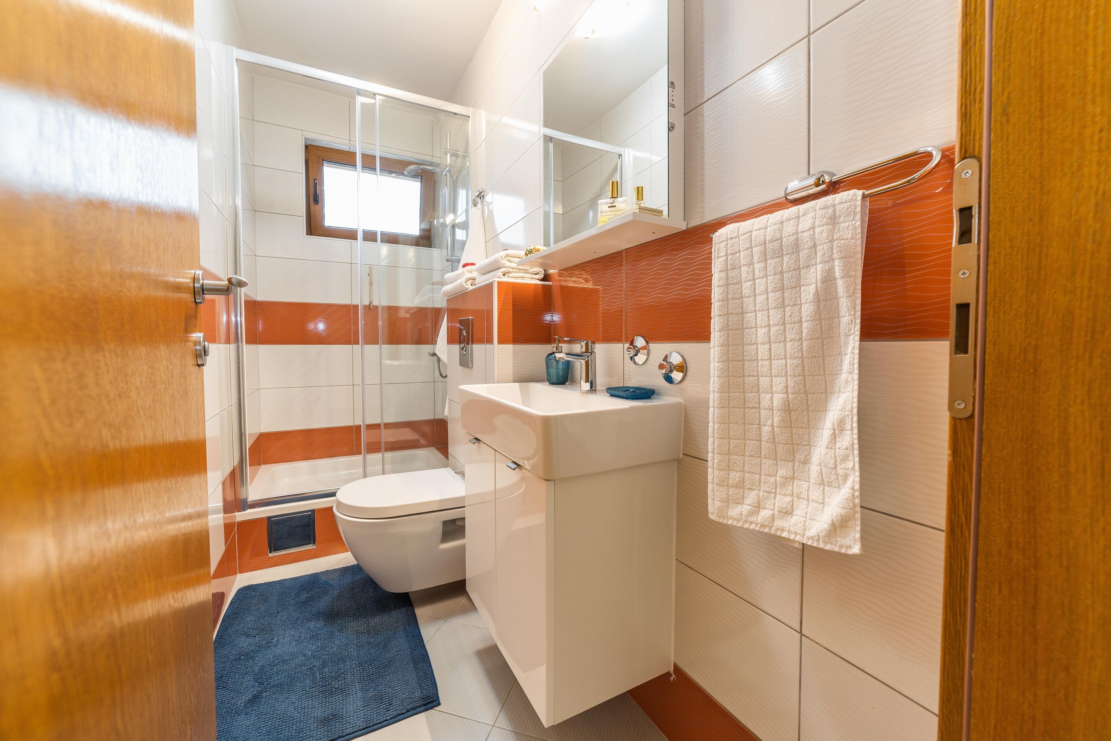 A modern bathroom with a glass shower enclosure, a white sink, and a blue bath mat.
