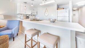 Una cocina moderna con armarios blancos, luces colgantes, microondas integrado y refrigerador.