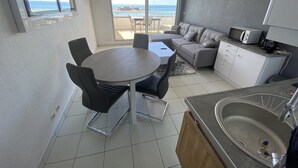 Un espacio habitable compacto con comedor, kitchenette y un balcón con vistas al mar.