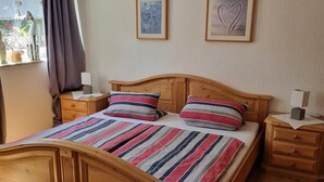 Uma cama de madeira com roupa de cama listrada, duas mesas de cabeceira e quadros na parede.