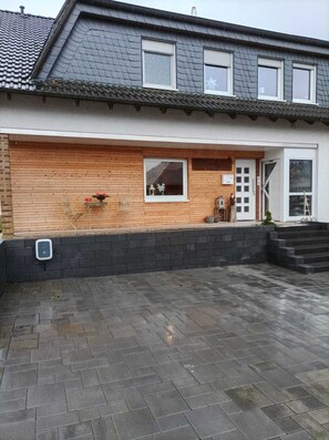 Une maison à deux étages, avec un toit en tuiles, une façade en bois et des fondations en briques.