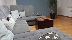 A modern living room with a grey sectional sofa, a wooden coffee table, and a potted plant. - Large family-friendly apartment for 2 - 5 people on the first floor. (Rheinland-Pfalz - Beuren (Eifel))