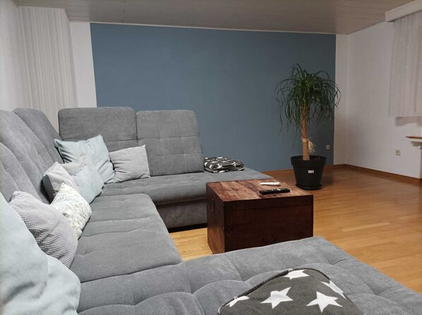 Una sala moderna con un sofá seccional gris, una mesa de centro de madera y una planta en maceta.