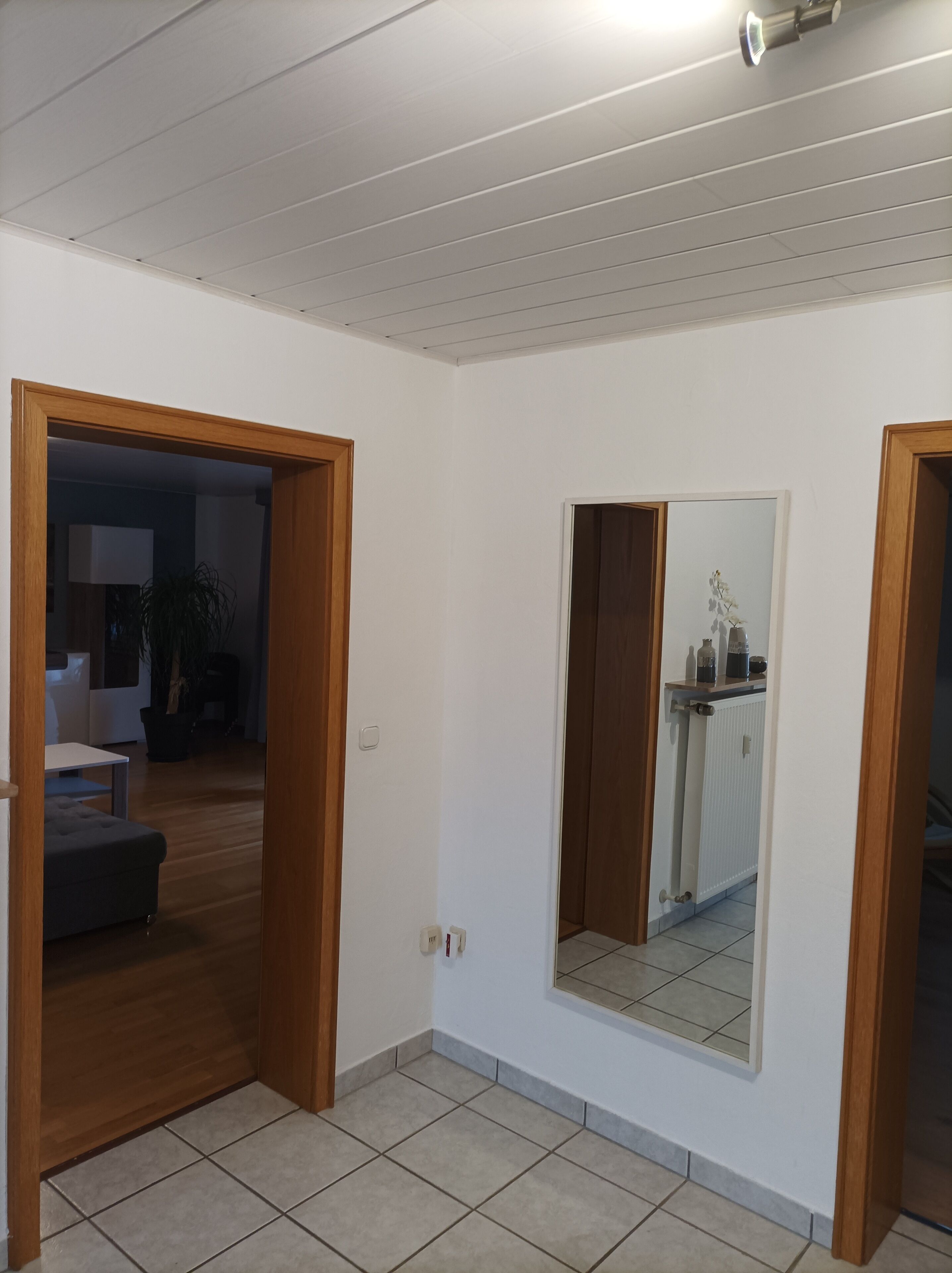 Un pasillo con puerta de madera, un espejo y suelo de baldosas.