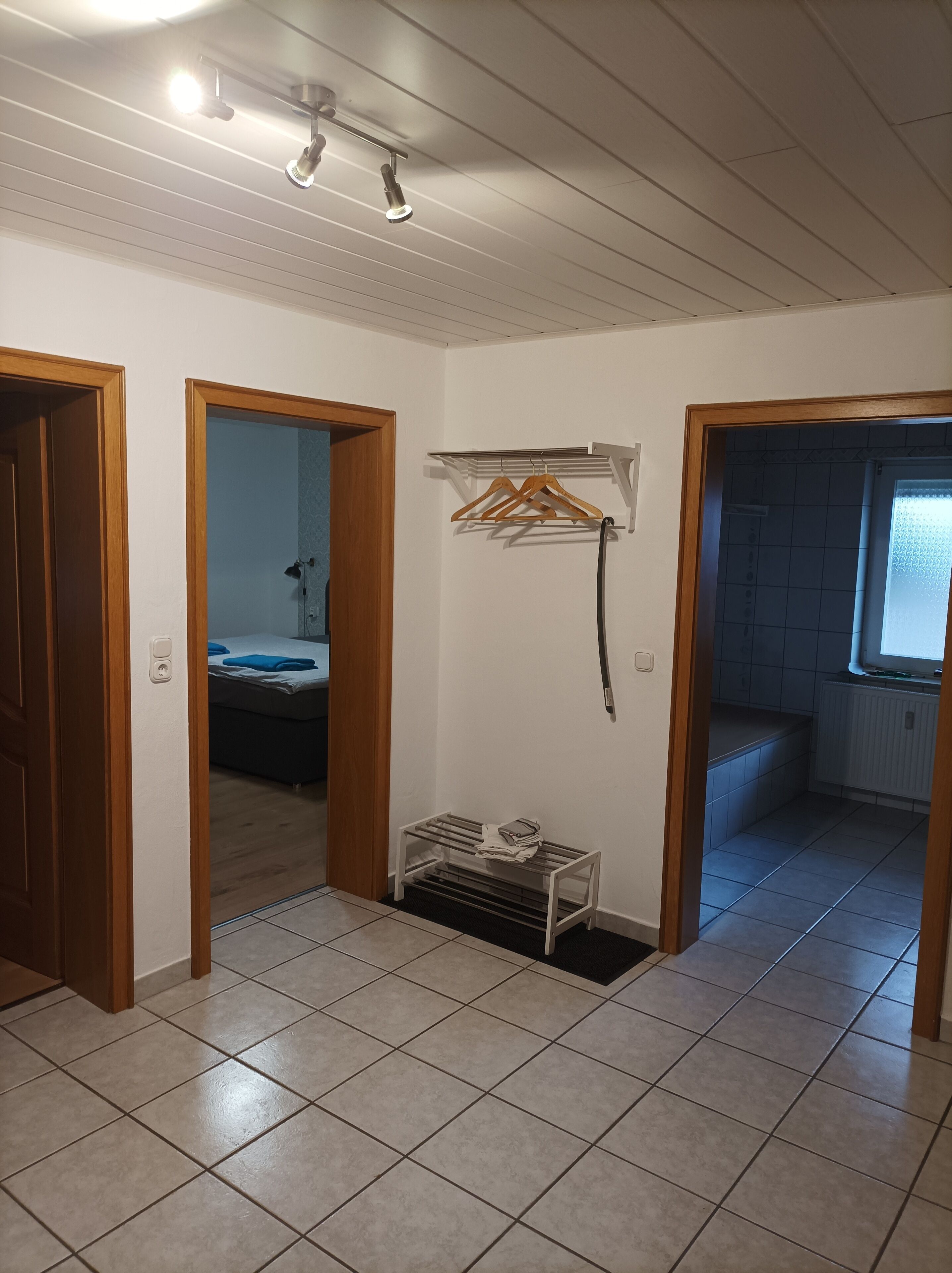 A room with a tiled floor, a bed in the background, a drying rack, and a radiator.
