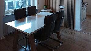 A modern dining area with a wooden table and chairs, a window with a view of the outside, and a kitchen visible through an archway. - Large family-friendly apartment for 2 - 5 people on the first floor. (Rheinland-Pfalz - Beuren (Eifel))