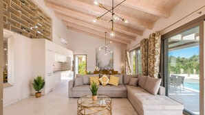 A modern living room with a sectional sofa, a glass coffee table, and a dining area with a view of the outdoors. - Villa Anemona - Zante Prime Heated Pool Villas  (Zakynthos)