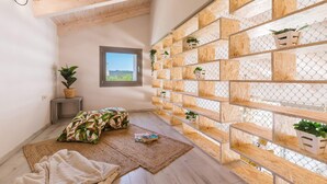 A cozy room with a sloped ceiling, a window with a view, a wooden bookshelf with plants, a patterned cushion, and a small table with a basket. - Villa Anemona - Zante Prime Heated Pool Villas  (Zakynthos)