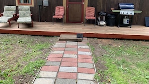 A wooden deck with two chairs, a grill, and a door.