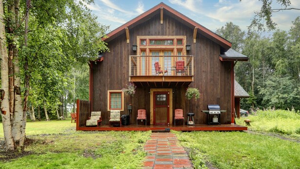 A rustic wooden cabin with a balcony, a brick pathway leading to the entrance, and outdoor seating.