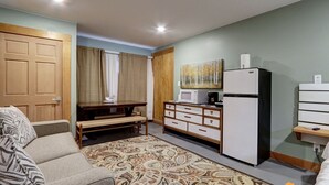 A compact living space with a sofa, a dining table, a kitchenette, and a bed.