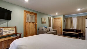 A bedroom with a large bed, a wooden bench, a sofa, a television, and a door with curtains.