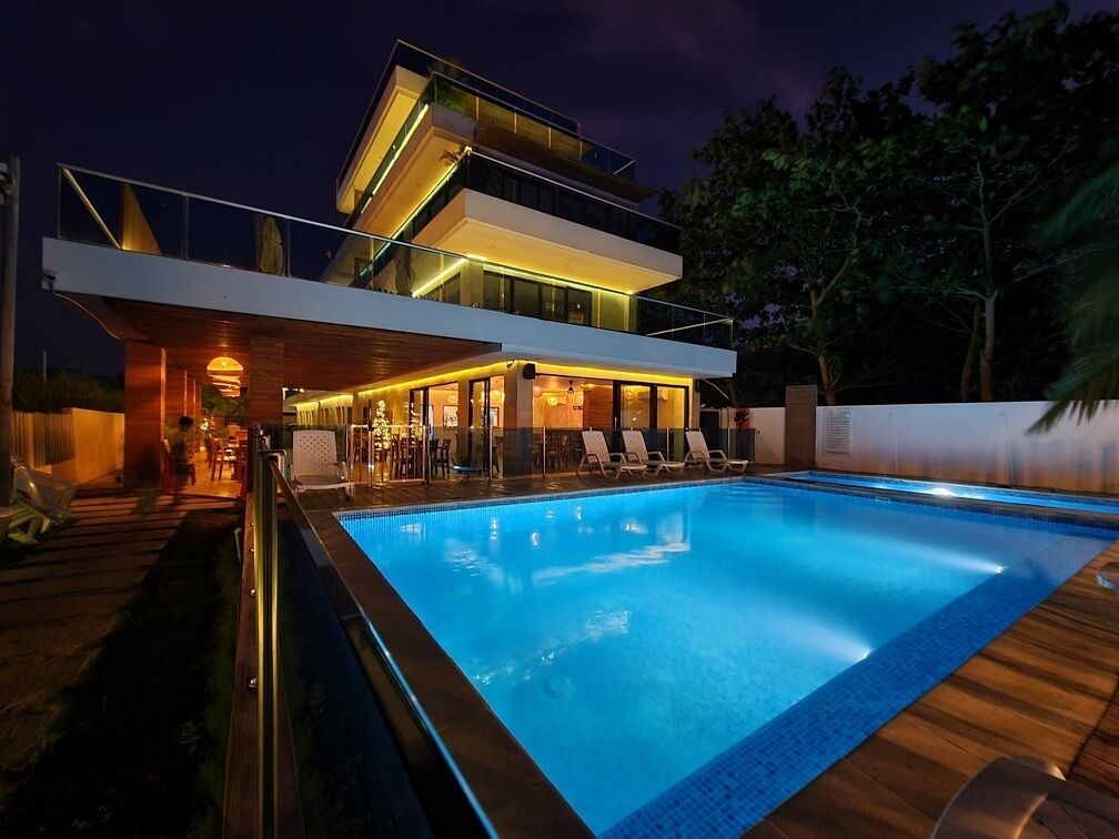A modern multi-story house with a swimming pool, outdoor seating, and a well-lit entrance.
