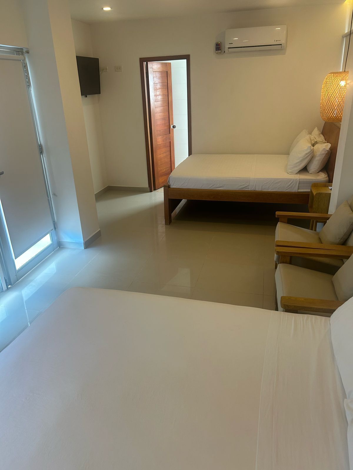 A bedroom with a bed, a chair, a wardrobe, and a door leading to another room.