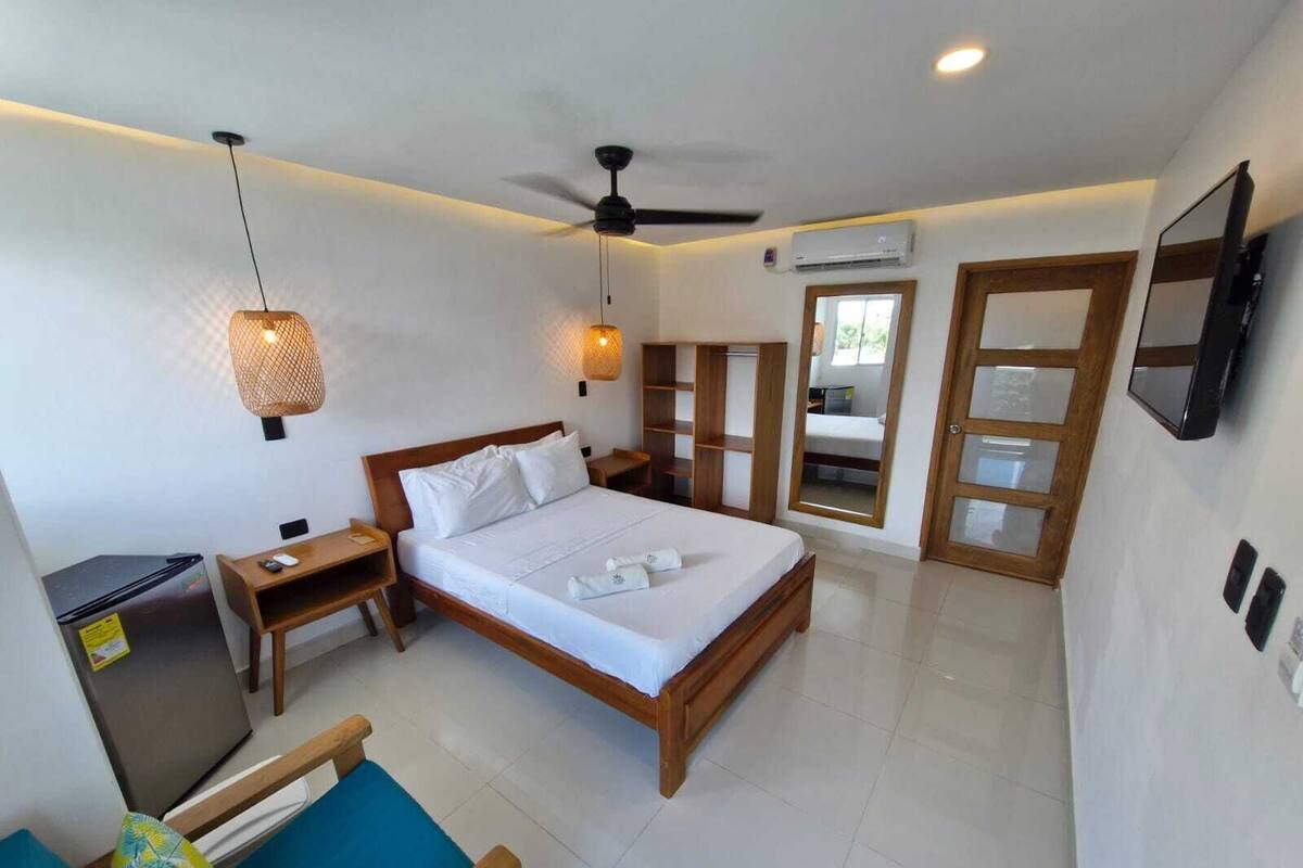 Une chambre d’hôtel comprenant un lit, des tables de chevet, un bureau, une chaise, un ventilateur de plafond, un appareil de climatisation et un téléviseur fixé au mur.