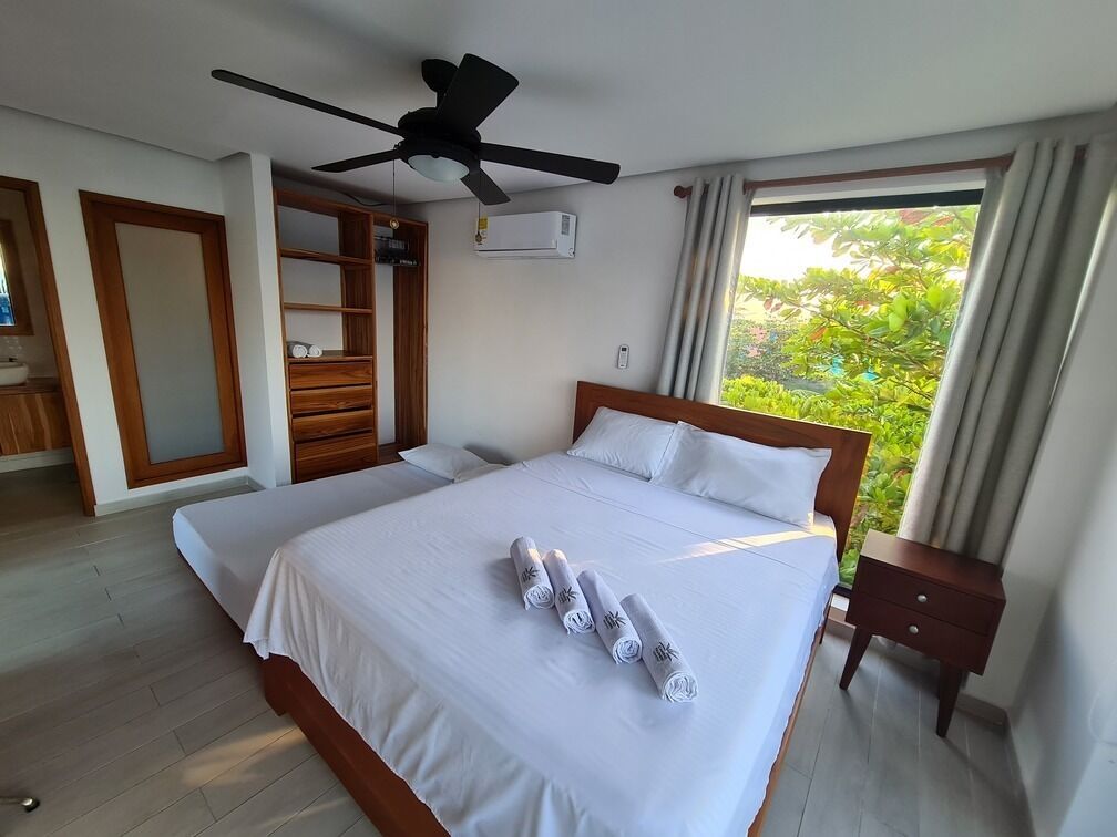 A hotel room with a large bed, a ceiling fan, a window with curtains, and a wooden wardrobe.