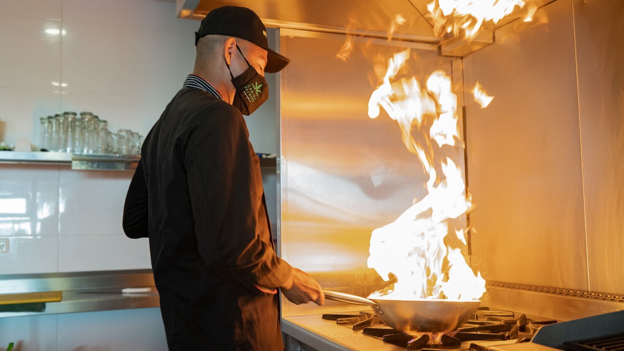 A chef cooking with a large flame on a stove in a modern kitchen.