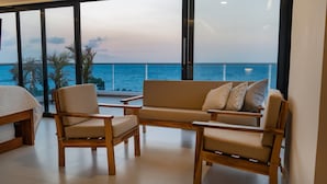 Una habitación moderna con un ventanal grande con vistas al océano, un sofá, dos sillones y una cama.