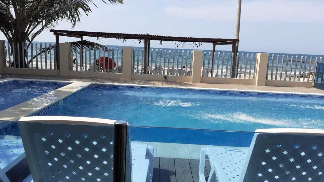 Un espace piscine avec vue sur la plage, une pergola et une clôture.