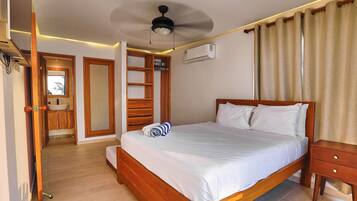 Habitación de hotel con una cama de madera, una mesita de noche, un ventilador de techo y un equipo de aire acondicionado.