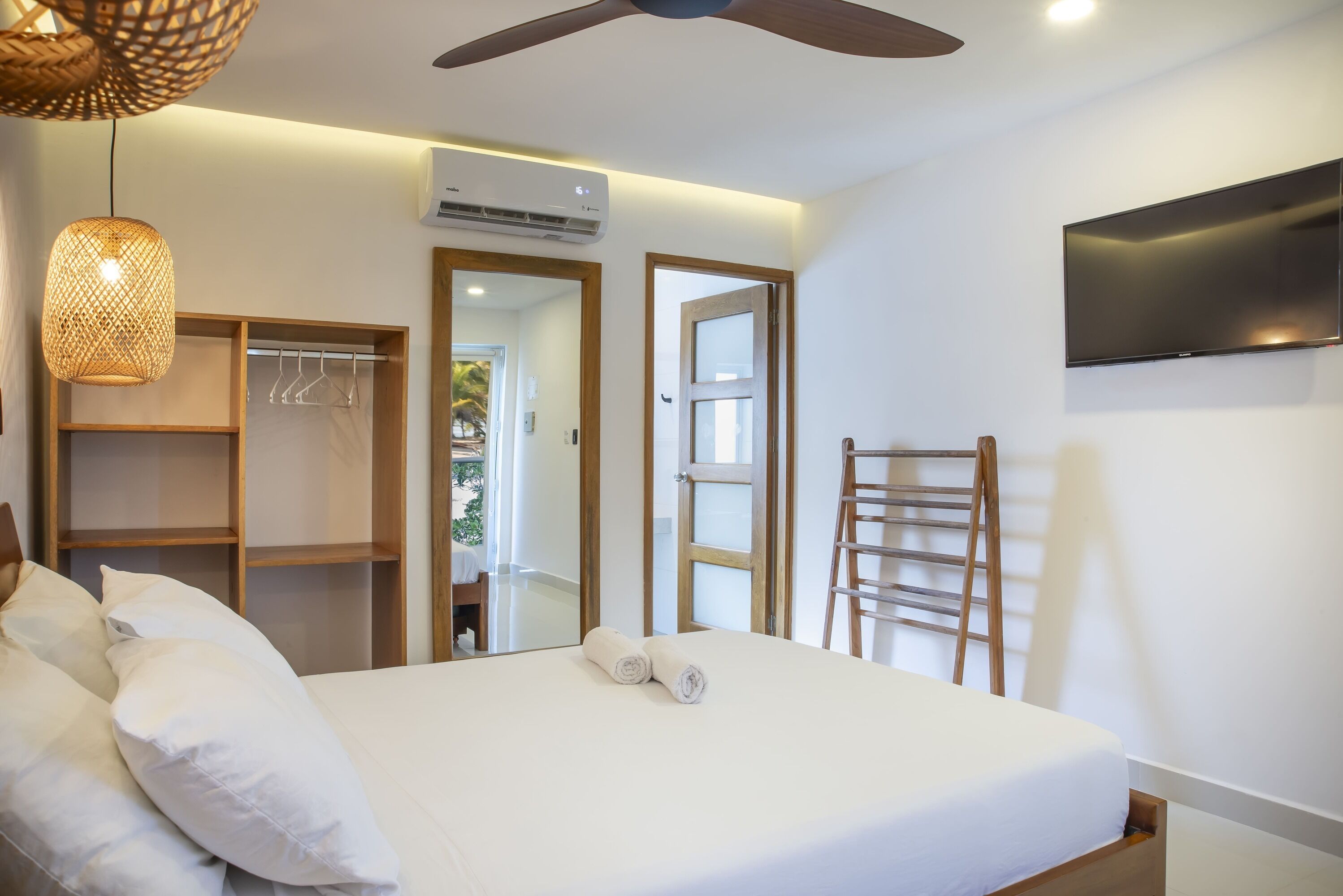 Quarto com cama, guarda-roupa, espelho, televisão e ventoinha no teto.