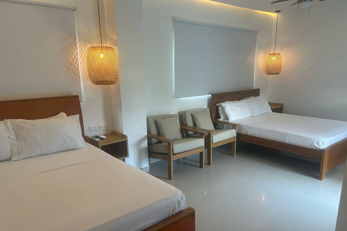 Une chambre d’hôtel avec deux lits, une chaise et deux lampes suspendues.